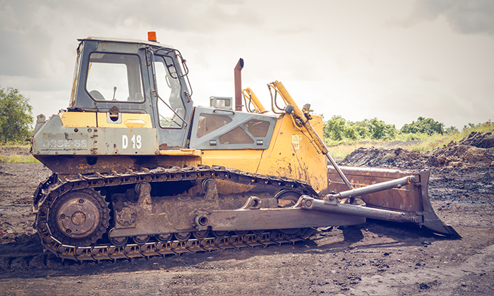 a photo of a yellow excavator in an industrial area with gravel on a cloudy day