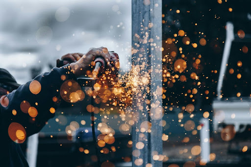 How to Spec Power Resistors for Real-World Industrial Applications 3 A close-up of an industrial worker generating a shower of bright orange sparks while grinding or welding a metal structure.