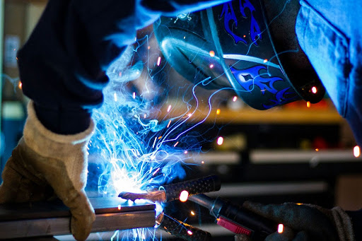 How to Spec Power Resistors for Real-World Industrial Applications 4 A close-up of a worker wearing a protective welding helmet and heavy gloves, actively welding a metal joint with a bright blue arc and sparks.