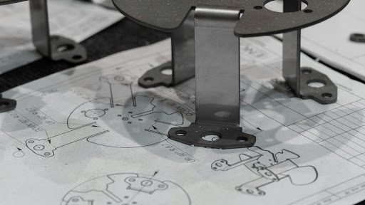 How to Spec Power Resistors for Real-World Industrial Applications 6 A metal bracket component resting directly on top of a printed engineering blueprint and technical schematic.
